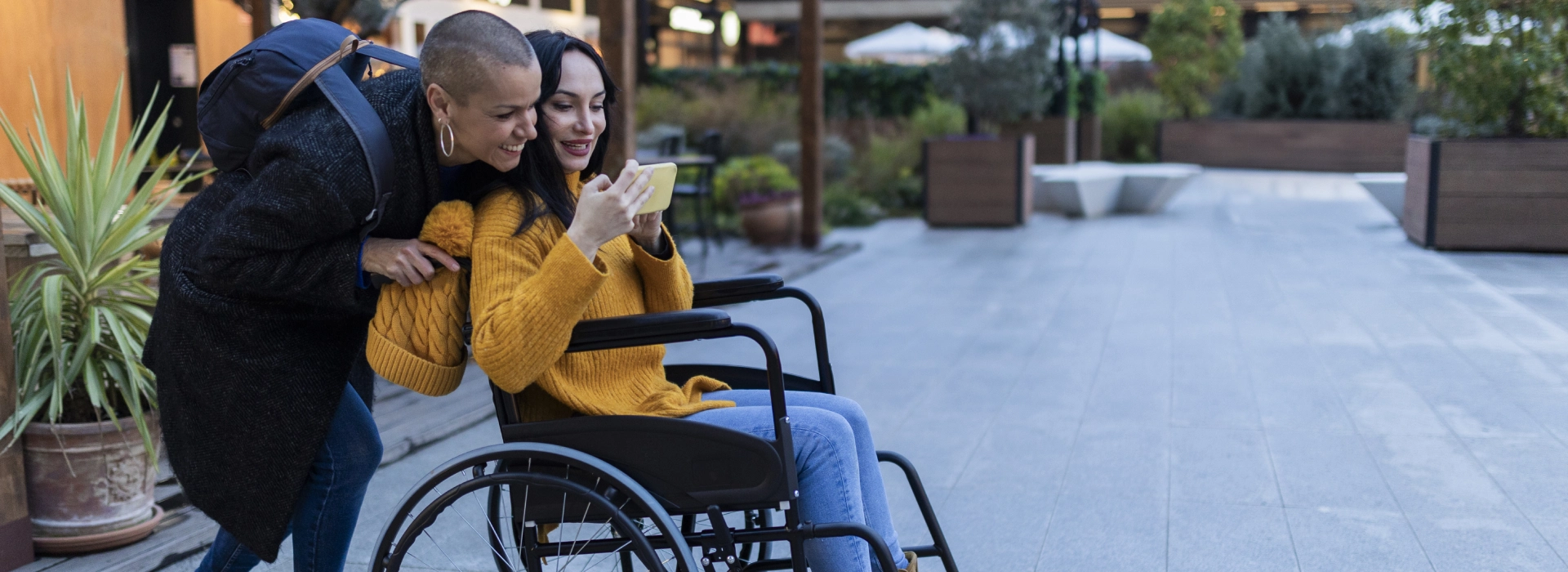 Two women in a wheelchair looking at their cell phone.
