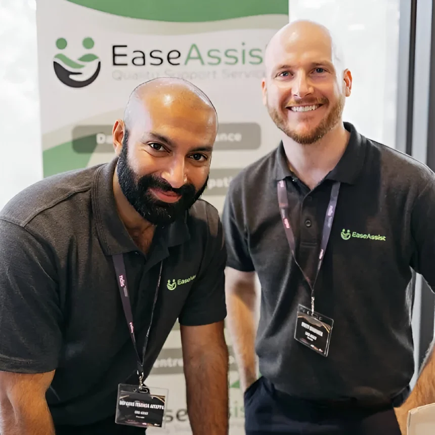 Two men in dark polo shirts stand in front of an EaseAssist banner. They are smiling and wearing lanyards with name tags.