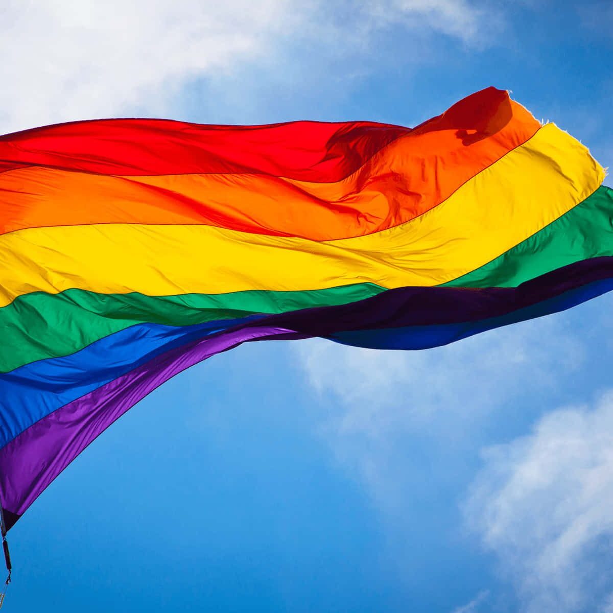 A rainbow flag flying in the sky on a sunny day.